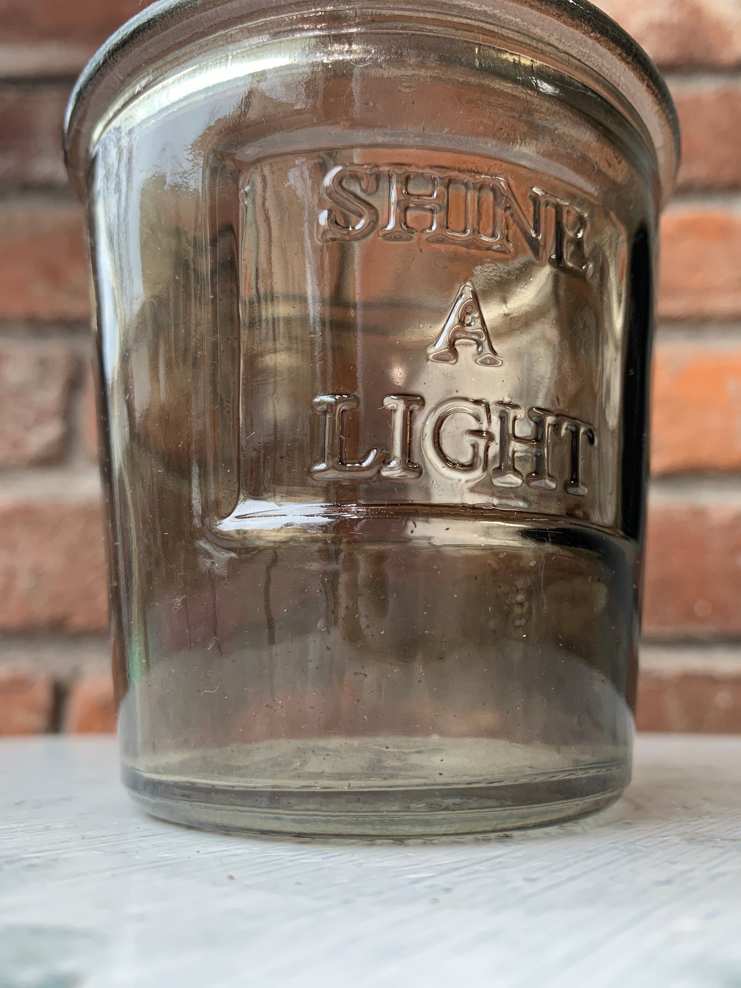 Gray glass votive holder that reads, "Shine A Light".